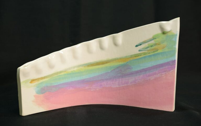 Curved ceramic piece with pastel rainbow brushstrokes and small indents, set against a black background.