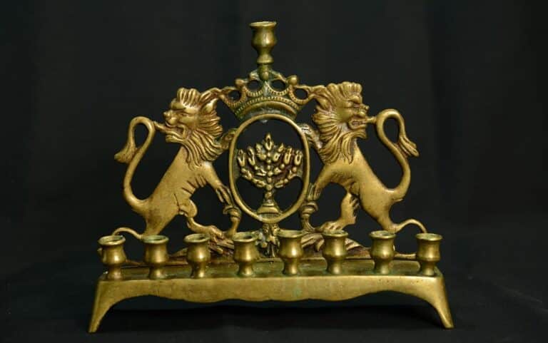 Brass menorah with two lions flanking a central emblem and eight candle holders on a black background.