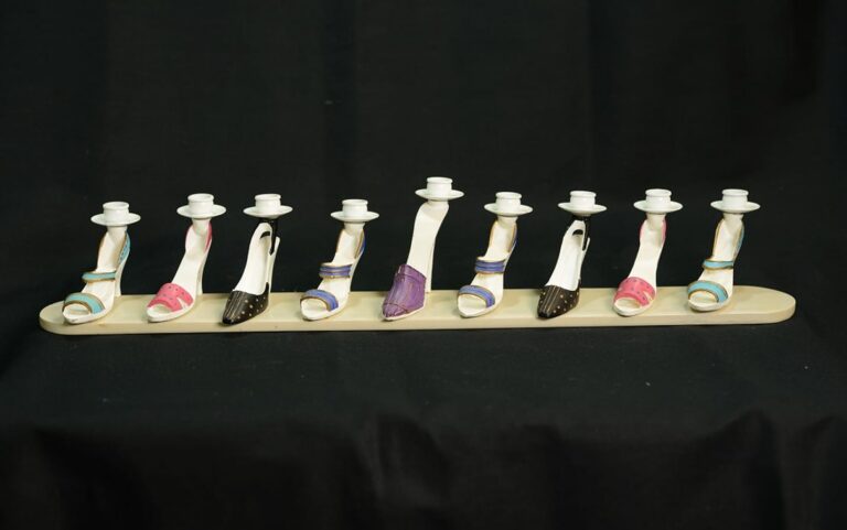 A candle holder with eight high-heeled shoe-shaped candle inserts on a beige base against a black background.