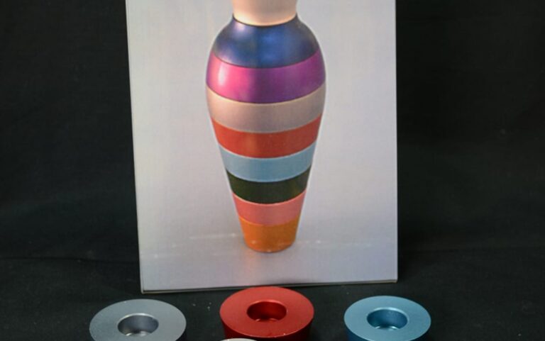 A photo of a striped, colorful vase with three round objects in silver, red, and blue in front of it.