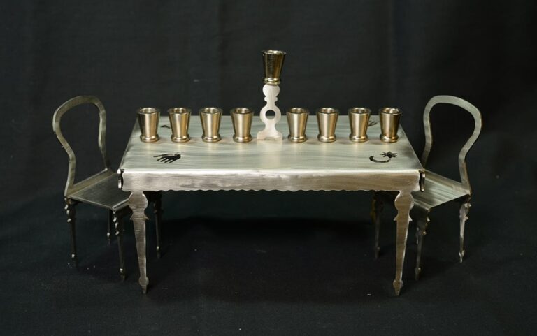 Metal table with nine cups, a white candlestick, two chairs, and black sun and moon symbols on the tabletop.