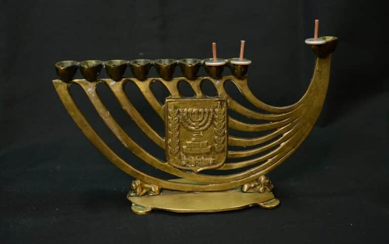 Brass menorah with seven candle holders and a crest in the center, set against a black background.