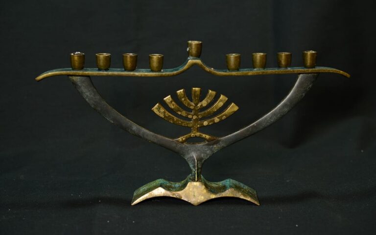 A metal menorah with nine candle holders and a gold decorative detail, set against a black background.