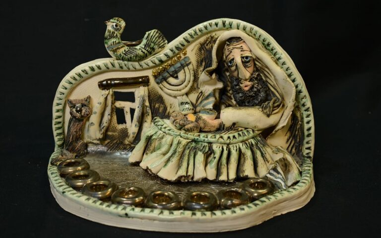 Ceramic menorah featuring a bearded man at a table, a cat, a rooster, and a window, all against a dark background.