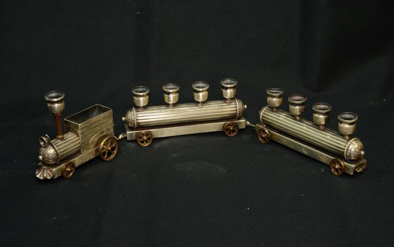 Metal toy train with two passenger cars, each holding four shot glasses, on a black background.