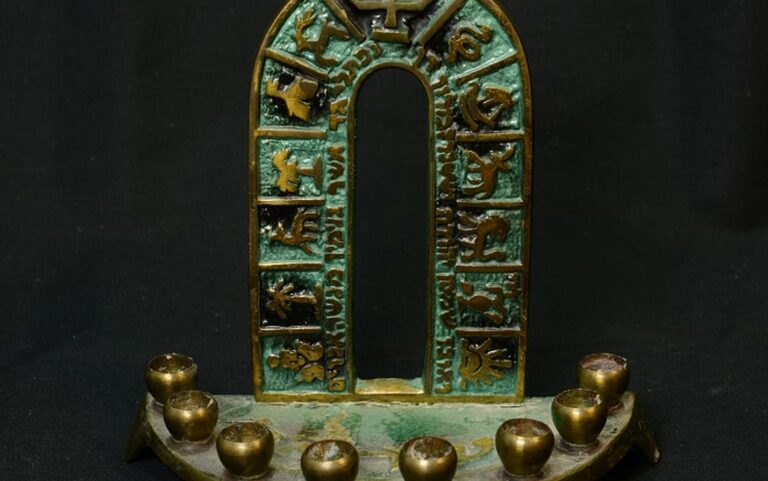 Bronze Hanukkah menorah with Hebrew letters and animal symbols on a decorated arch, set against a black background.