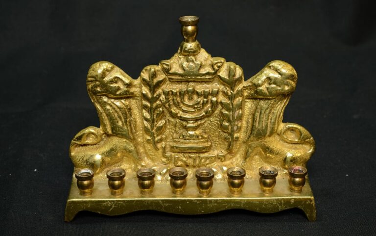 A gold Hanukkah menorah with two lion figures and nine candle holders, set against a black background.
