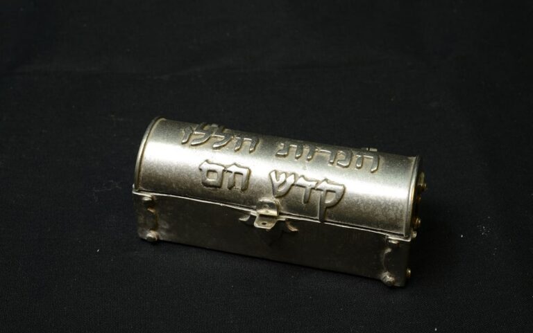 A small metallic box with Hebrew inscriptions on the lid, set on a black background.