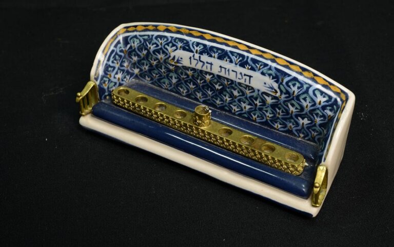 A decorative menorah with blue and gold patterns on ceramic, featuring Hebrew text above the candle holders.