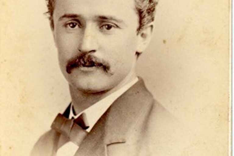 Sepia portrait of a young man with curly hair, mustache, suit, and bow tie, looking directly at the camera.