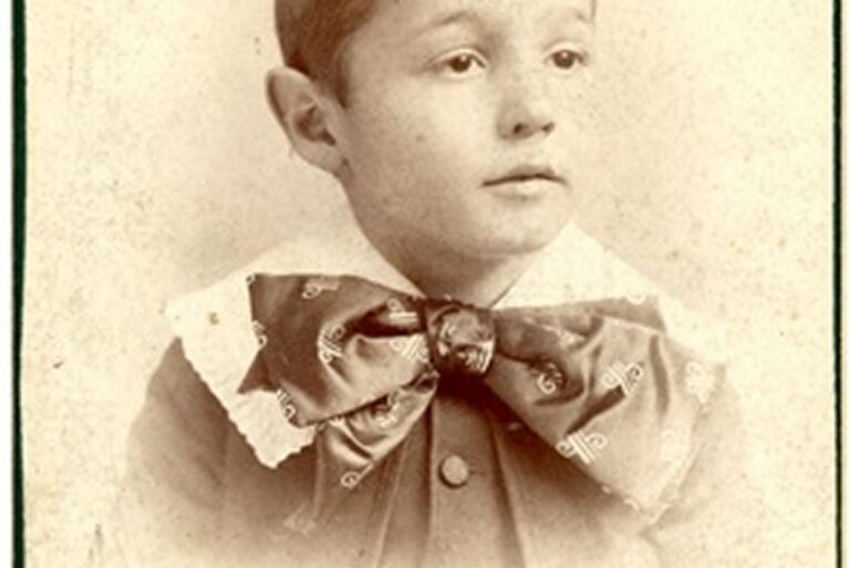 Sepia photograph of a young boy with short hair, wearing a large bow tie and a collared shirt.