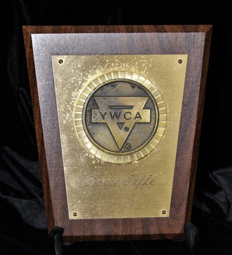 YWCA plaque with a circular emblem on a gold plate mounted on a wooden base, engraved with the name “Dorie Jaffe.”.