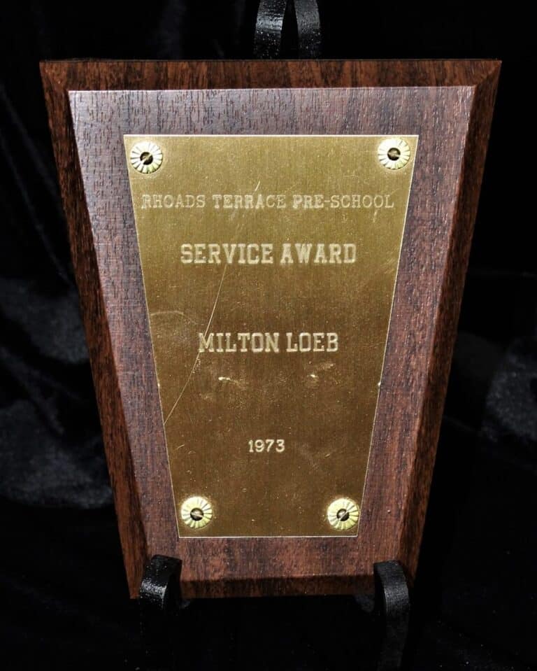 A wooden plaque with a gold plate reading “Service Award, Milton Loeb, 1973, Rhoads Terrace Pre-School.”.