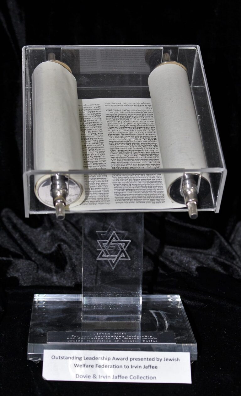 A Torah scroll displayed on a clear stand with a Star of David and an award plaque at the base.