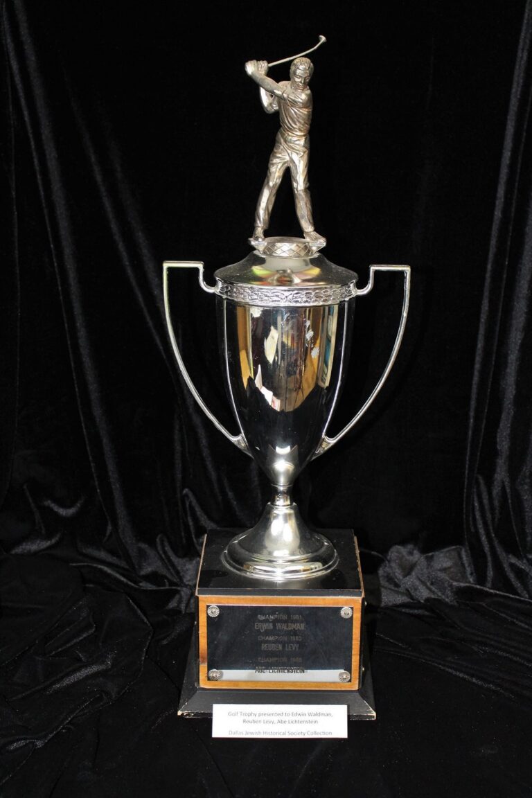 Silver golf trophy with golfer figurine on top, displayed on a black cloth background, with an engraved plaque at the base.