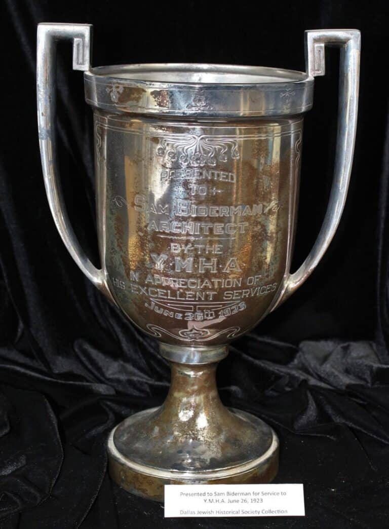 Silver trophy cup with engraved text, presented for service, displayed on a black cloth with a small label in front.