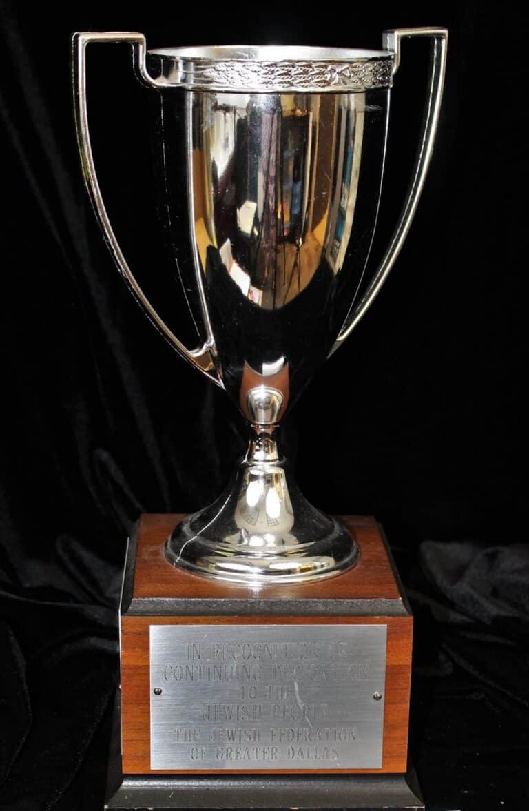 Silver trophy with two handles on a wooden base, featuring an engraved plaque on the front.