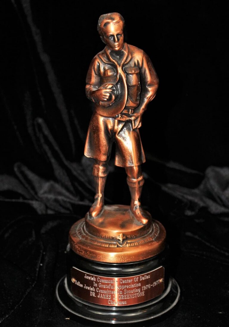 Bronze statue of a man holding a hat, mounted on a round base with an engraved plaque at the bottom.