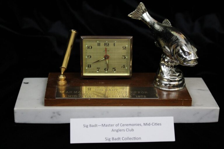 A desk clock on a marble base with a fish figurine, a pen, and label for Sig Badt, Mid-Cities Anglers Club.