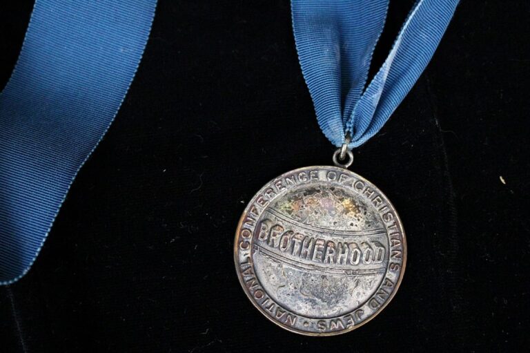 A silver medal with “BROTHERHOOD” on a blue ribbon, lying on a black background.