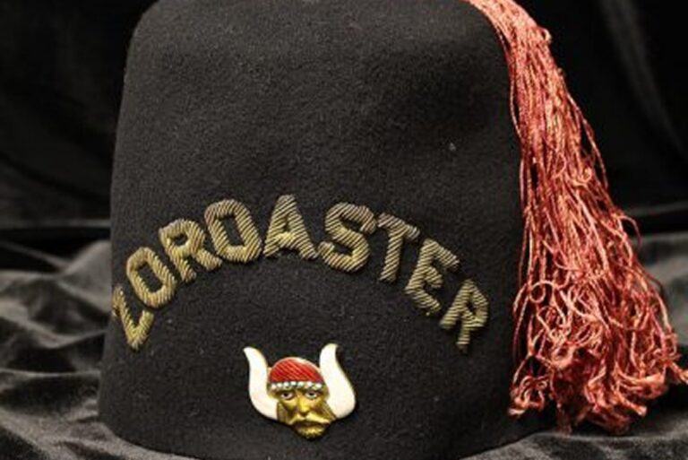 A black fez with “ZOROASTER” in gold letters, a red tassel, and a gold face pin with white horns.