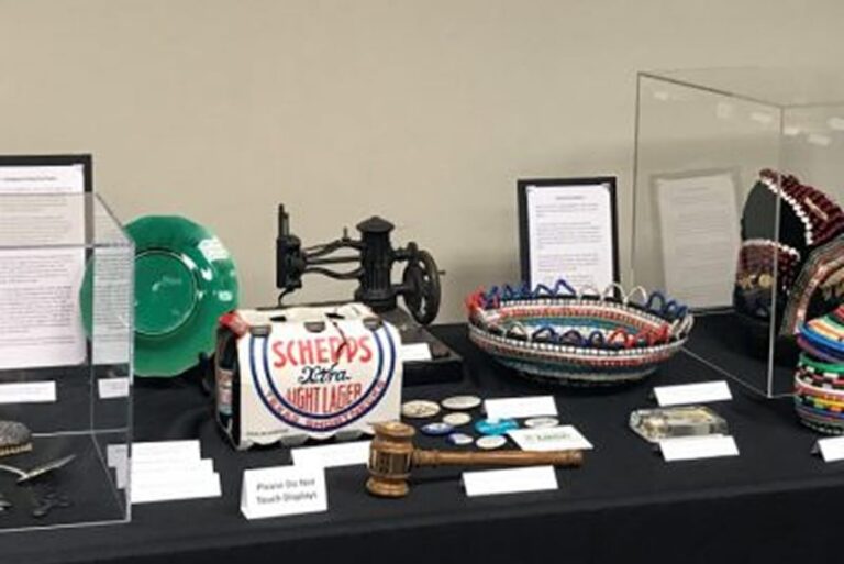 Table display of vintage objects, baskets, a green plate, an old sewing machine, and a Schell’s beer box.