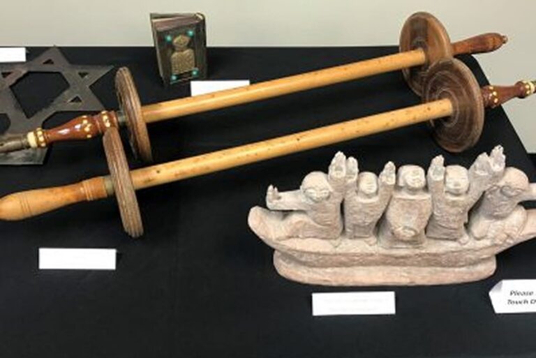 Two wooden Torah scroll rollers, a Star of David, a small book, and a carved boat with figures are displayed on a table.