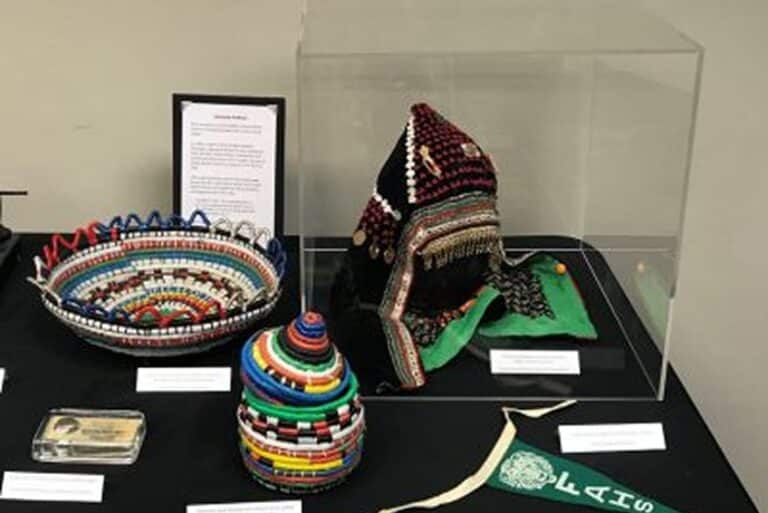 Colorful beaded baskets, a decorated hat in a display case, and informational placards on a black table.