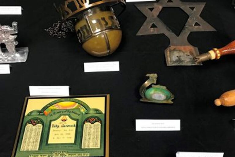 A display of Jewish artifacts, including a menorah, star of David, and Hebrew-inscribed plaque on a black cloth.