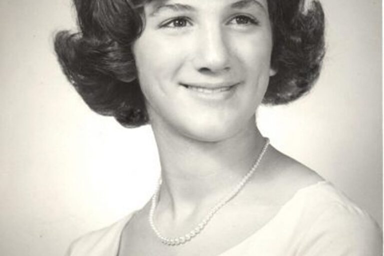 Black and white portrait of a young woman with short hair, wearing a blouse and pearl necklace, smiling slightly.