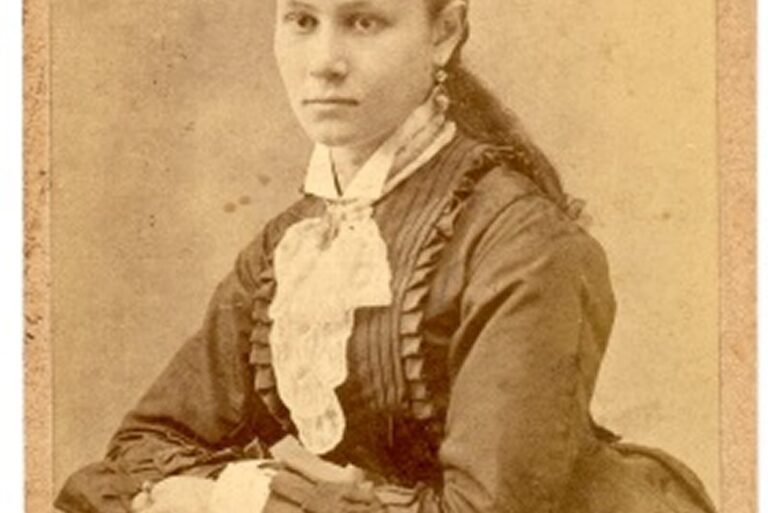 Young woman in 19th-century dress sits posing for a sepia-toned portrait with a serious expression.