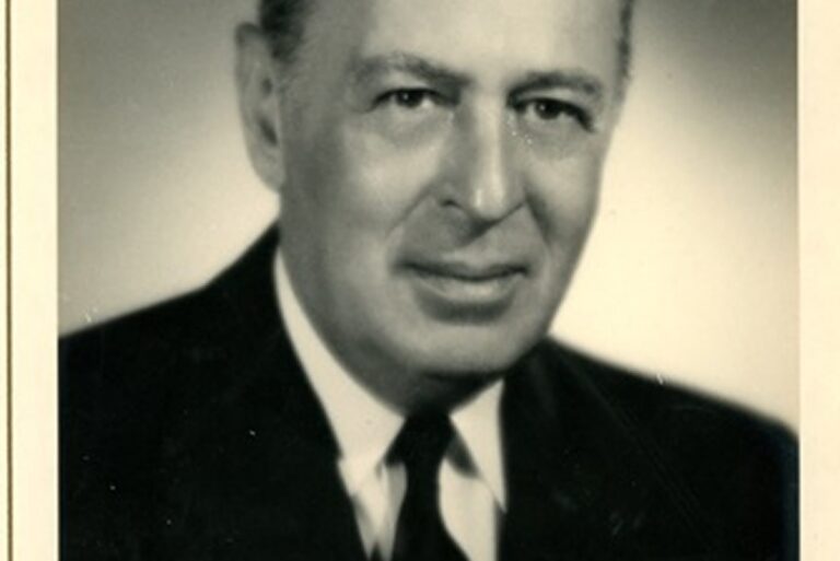 Black and white portrait of an older man in a suit and tie, facing forward and smiling slightly.