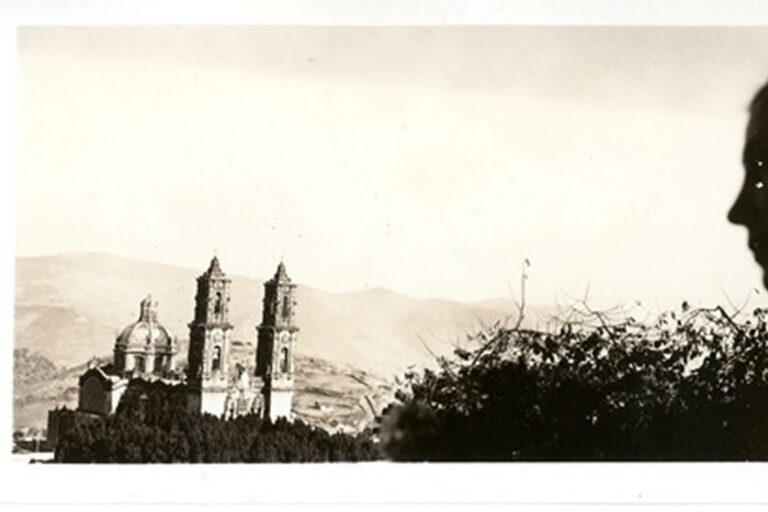 Silhouette of a person’s profile with a distant church and mountains in the background under a clear sky.