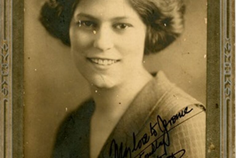 Sepia portrait of a smiling woman with wavy hair, wearing a suit jacket, and handwritten note at the bottom.