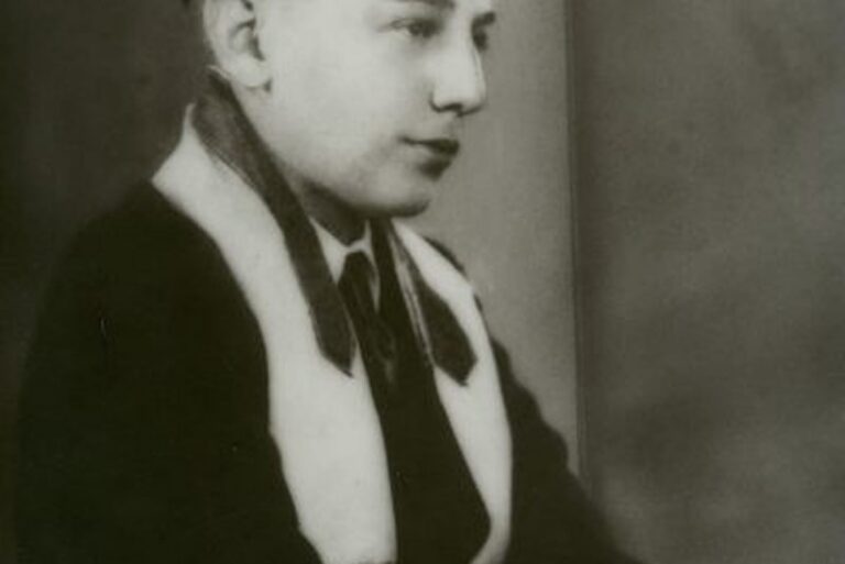 Black and white portrait of a young person in a suit, looking to the side, with a neutral background.