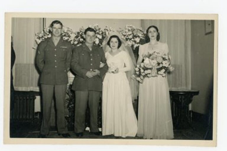 Black and white photo of a bride, groom, bridesmaid, and groomsman posing indoors with flowers.