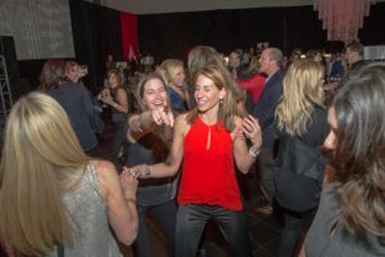 People dancing and smiling at an indoor party, with women in the foreground enjoying themselves.