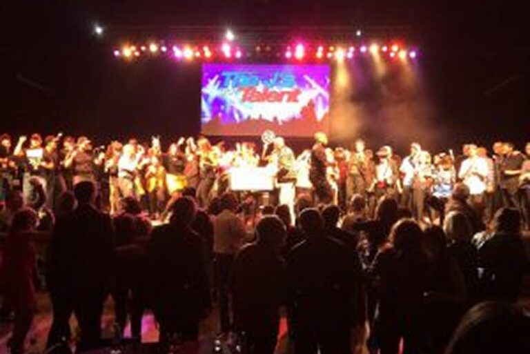 A large group of people on stage under colorful lights, with a “Texas Talent” sign in the background.