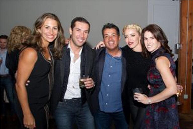 Five people pose together at a social event, smiling at the camera, some holding drinks.