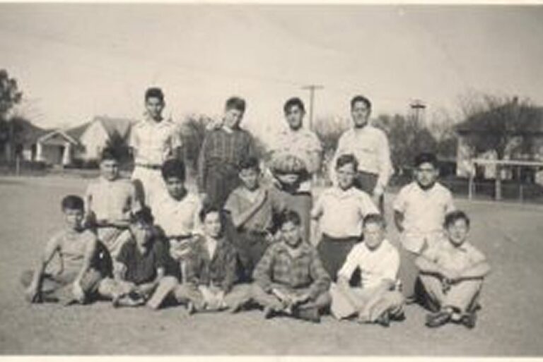 A group of boys poses with a football on a grassy field, with houses and trees visible in the background.