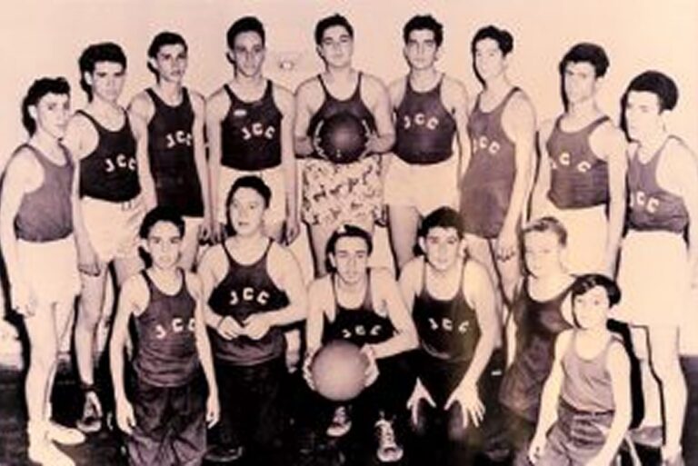 Vintage photo of a boys’ basketball team in matching uniforms, posing indoors with two basketballs.
