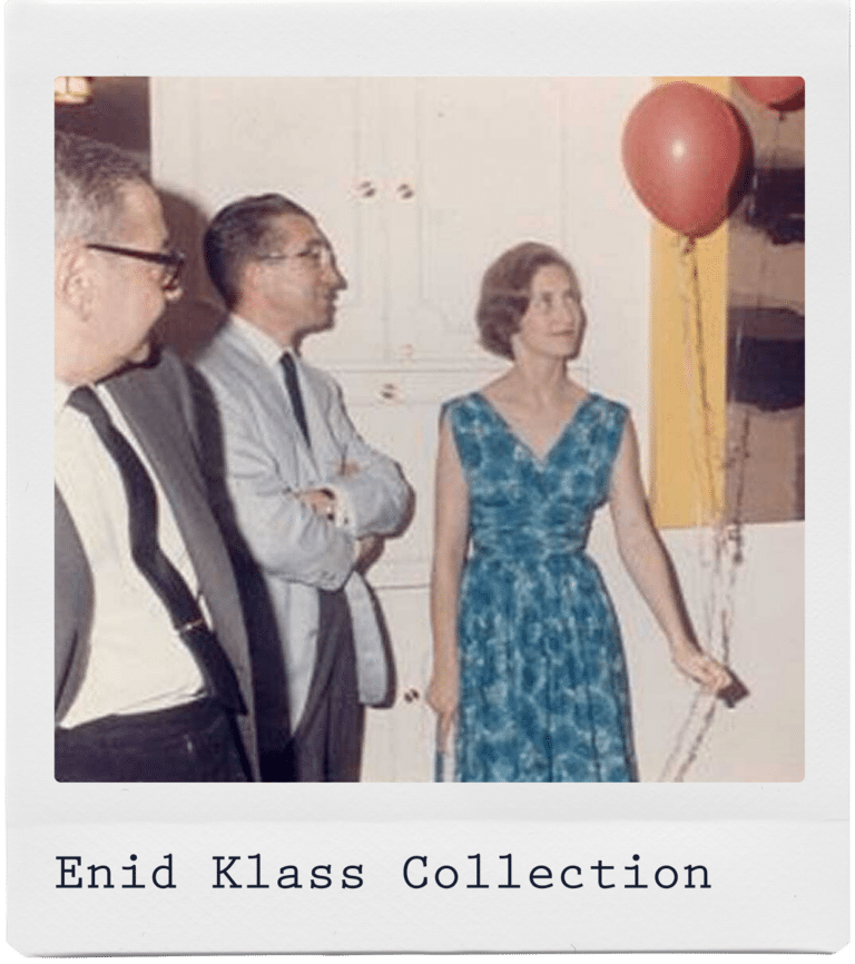 Three adults stand indoors; a woman in a blue dress holds a string tied to two red balloons.