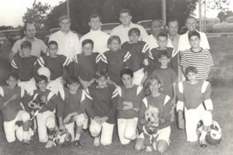 A vintage black-and-white photo of a youth football team, with coaches standing behind the players outdoors.