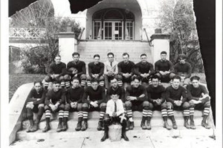 Vintage photo of a football team in uniforms sitting on steps, with a building in the background.