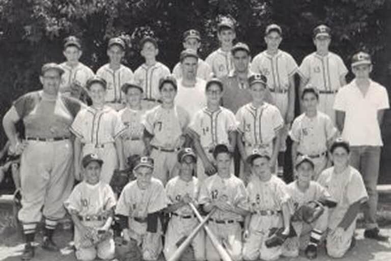Black and white photo of a youth baseball team posing with coaches, holding bats, wearing uniforms and caps.
